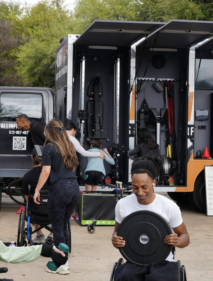 A participant lifting a weight while others train beside the mobile gym