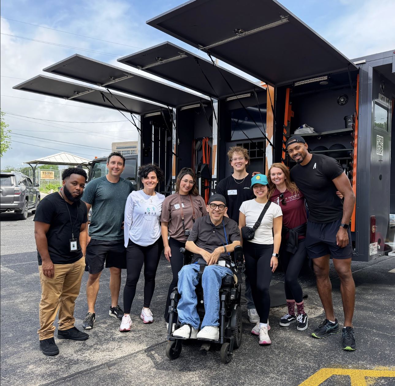 Participants and coaches, including a wheelchair user, posing together in front of the mobile gym
